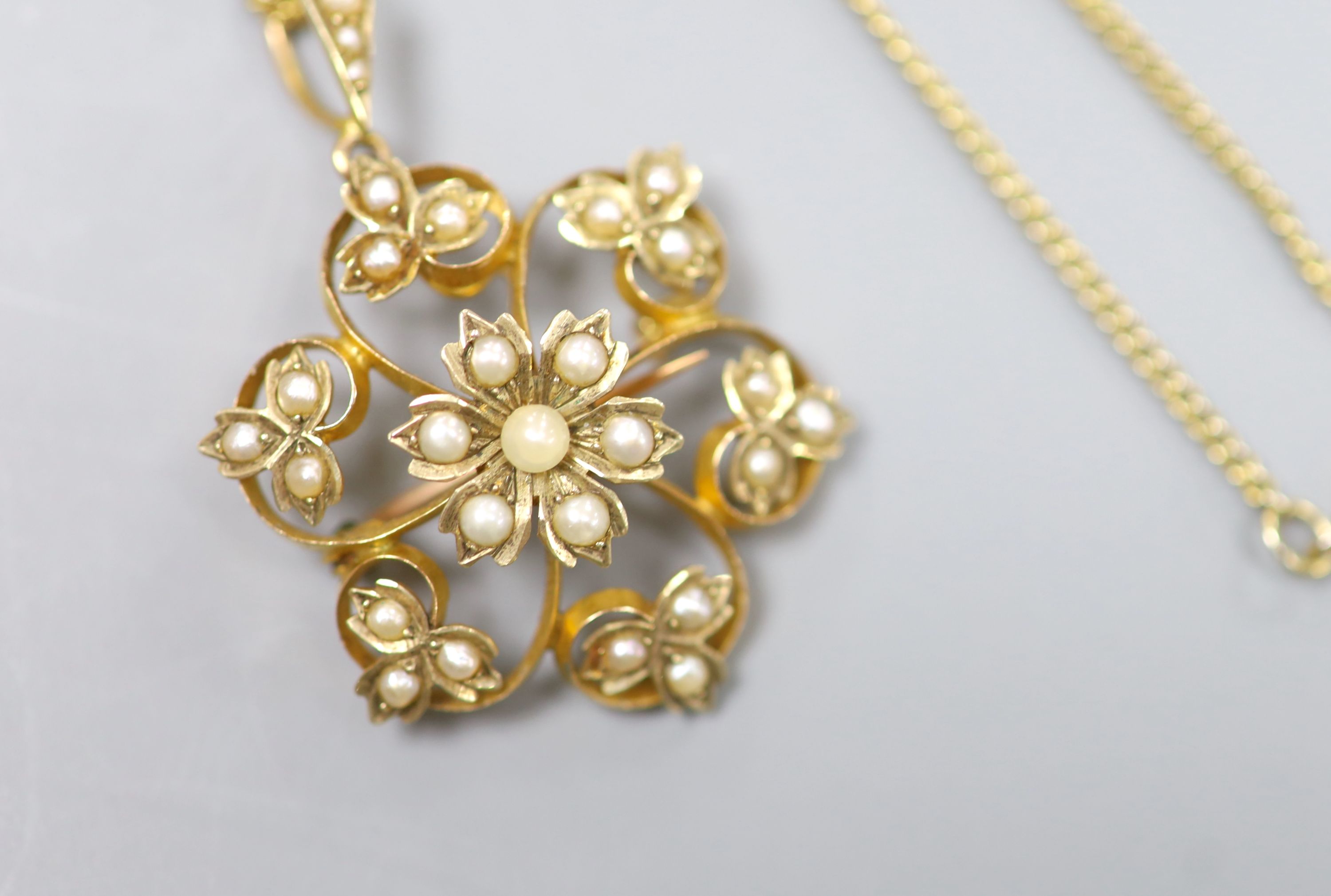 An Edwardian yellow metal and seed pearl set flower head pendant brooch